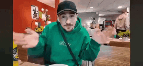a man wearing a green hoodie and a black hat is sitting at a table .