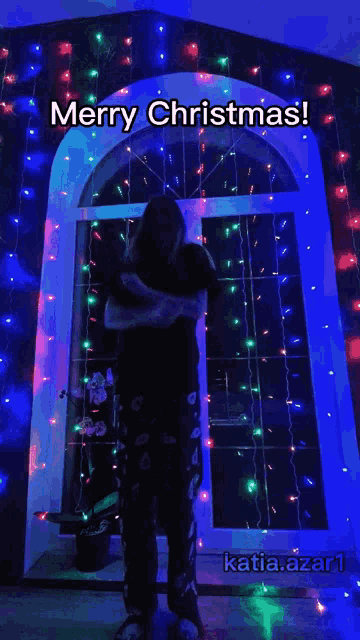 a person standing in front of a window with christmas lights behind them