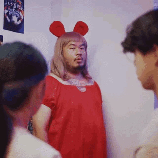 a man in a red dress and bunny ears stands in a room with other people
