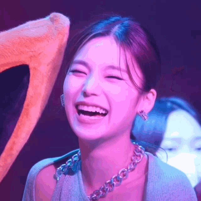 a close up of a woman laughing with her eyes closed while wearing a necklace .