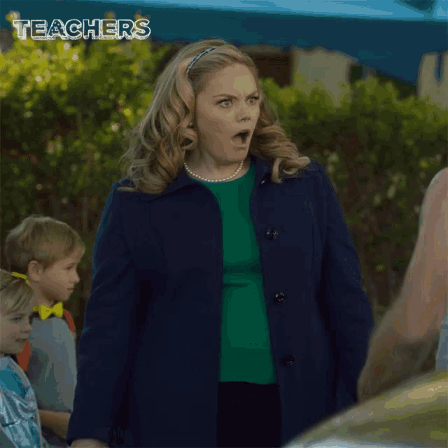 a woman in a blue coat and green sweater is holding her stomach and making a surprised face .