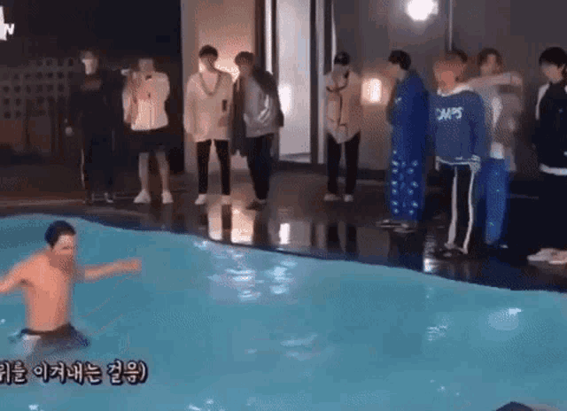 a group of people are standing around a swimming pool with a man swimming in it .