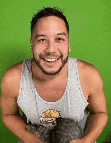 a man wearing a tank top with a hedgehog on it smiles while holding a cat