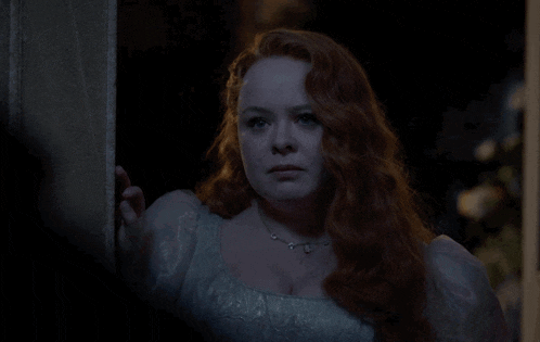 a woman with red hair and a white dress is standing in a dark room