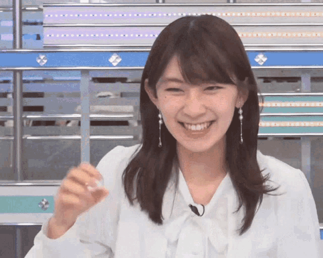 a woman wearing a white shirt and earrings smiles