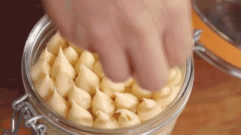 a close up of a person 's hand holding a jar filled with frosting .