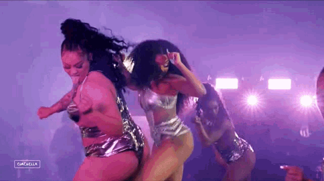 a group of women are dancing on a stage with purple lights .
