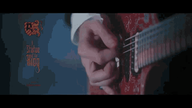 a close up of a person playing a guitar with a statue of a king logo behind them