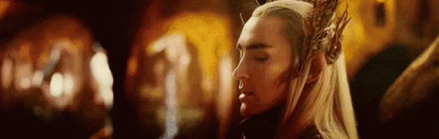 a man with long blonde hair and a crown on his head is standing in a dark room .