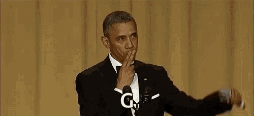 barack obama is giving a speech in front of a microphone while wearing a tuxedo .