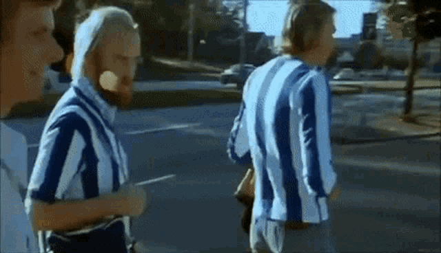 a man with a beard is walking down the street with two other men wearing blue and white striped shirts .