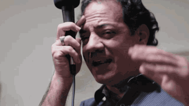 a man with a ring on his finger is holding a hair dryer to his head