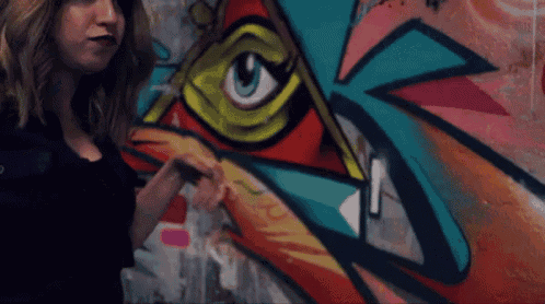 a woman stands in front of a wall with graffiti on it including an eye