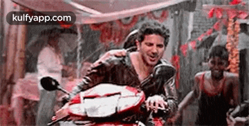 a man is riding a motorcycle in the rain while another man watches .