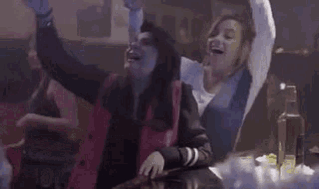 two women are dancing in a bar with their arms in the air .