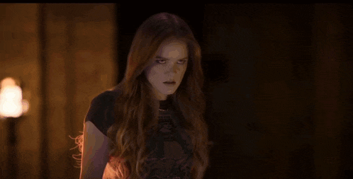a woman is standing in a dark room with fire coming out of her chest .