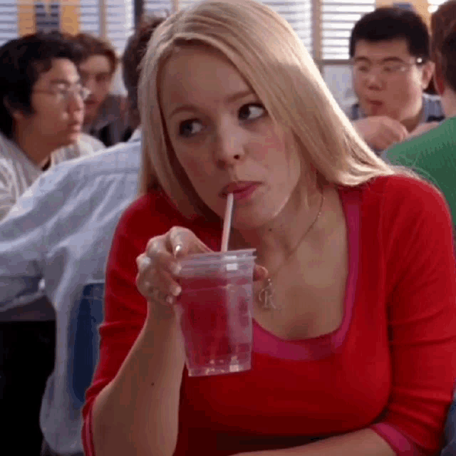 a woman in a red shirt is drinking from a cup with a straw .