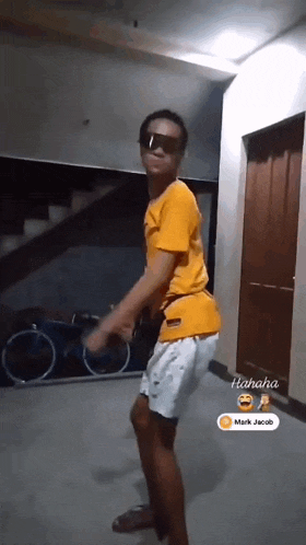 a man wearing sunglasses and a yellow shirt is dancing in a room with bicycles in the background .