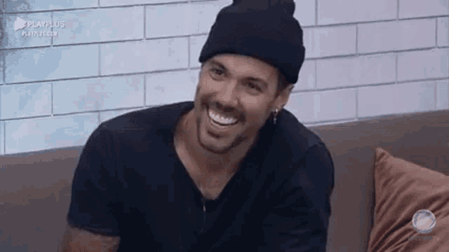 a man wearing a beanie is sitting on a couch and smiling .