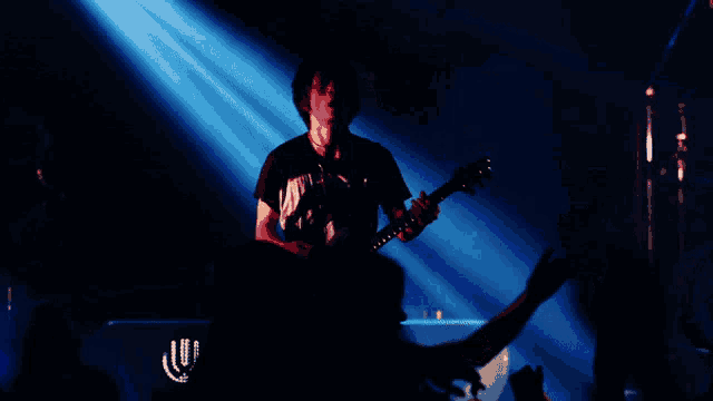 a person playing a guitar in a dark room with a blue light behind them