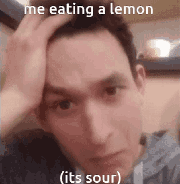 a man is holding his hand to his head while eating a lemon