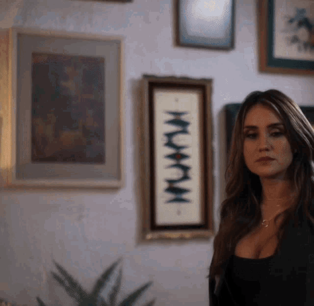 a woman stands in front of a wall with framed pictures on it and one of them says ' nmxm ' on it