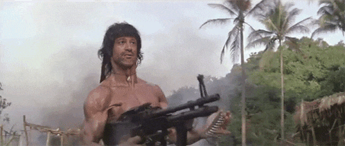 a shirtless man is holding a gun in a jungle .
