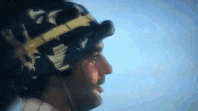 a close up of a man wearing a helmet and goggles against a blue sky