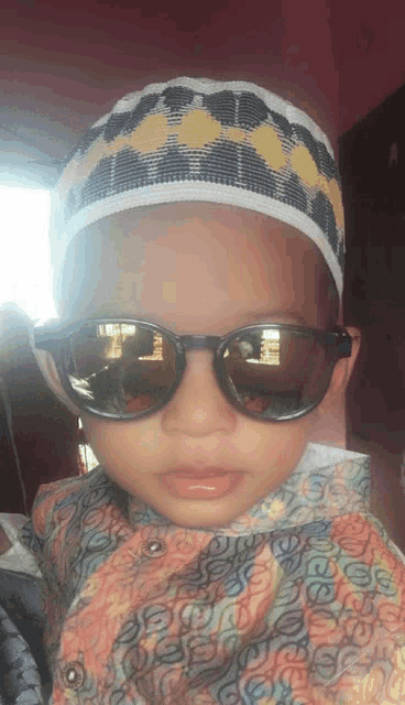 a young boy wearing sunglasses and a hat looks at the camera with his reflection in the sunglasses