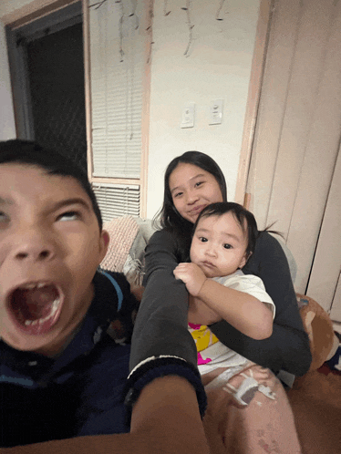 a boy making a funny face with his mouth open while a girl holds a baby