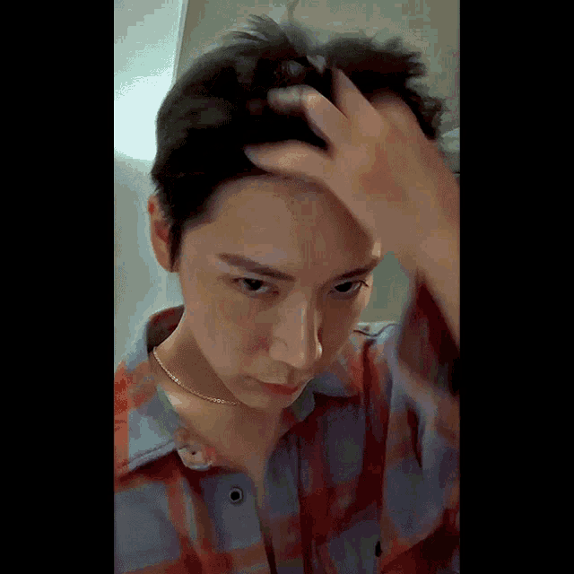 a man in a plaid shirt holds his hand to his forehead