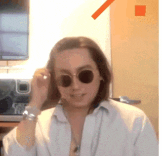 a woman wearing sunglasses and a white shirt is standing in front of a sign that says get yours