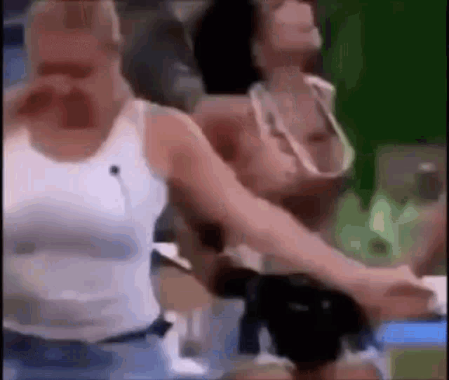 a man in a white tank top is holding a woman 's hand .