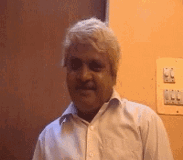 a man in a white shirt is standing in front of a wall with light switches