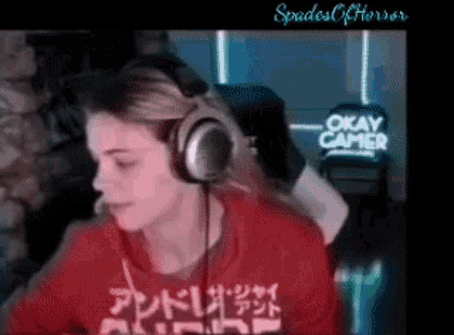 a woman wearing headphones is sitting in front of a sign that says " okay gamer "