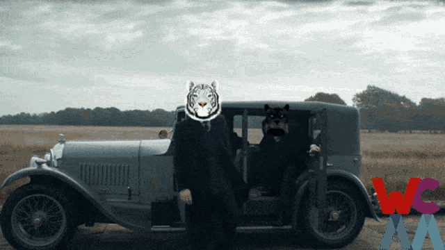 a man in a suit with a tiger mask on his head stands next to an old car