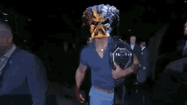 a man wearing a predator mask is holding a ufc championship belt