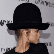a woman wearing a black hat with emporio armani written on the wall behind her