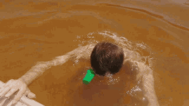 a man is swimming in a pool with a green bottle in his mouth