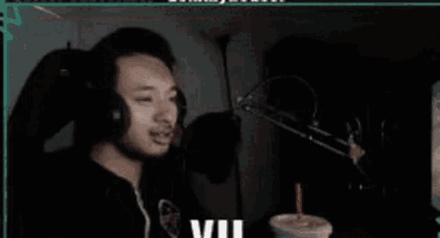 a man is making a funny face in front of a microphone while sitting in front of a cup of milkshake .