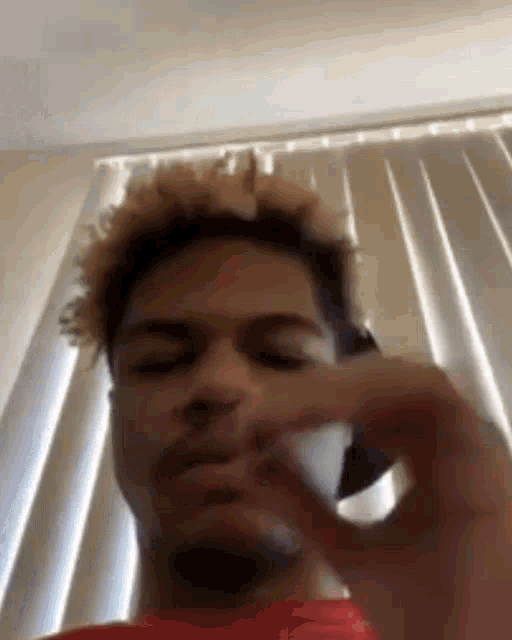 a man is talking on a cell phone in front of a window in a room .