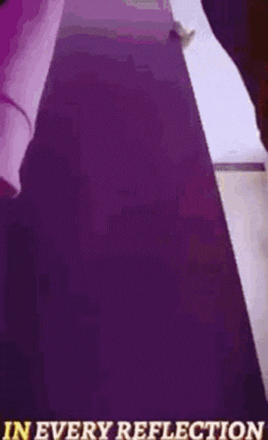 a person in a yellow suit is standing in front of a purple wall with the words in every reflection written on it .