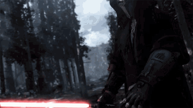 a person holding a red lightsaber in a forest