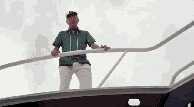 a man in a green shirt and white pants is standing on top of a boat .