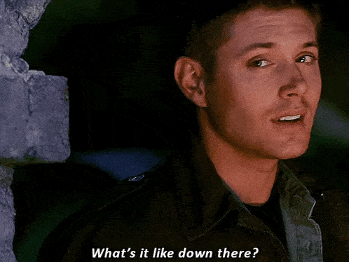 a man is standing next to a brick wall and says what 's it like down there ?
