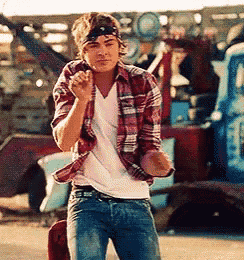 a young man in a plaid shirt and jeans is standing in front of a truck .