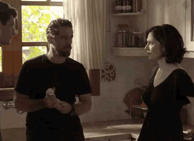 a woman in a black dress stands in a kitchen with two men