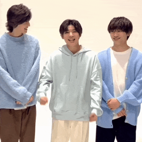 three young men wearing light blue sweaters and cardigans stand next to each other