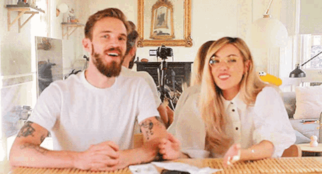 a man and a woman are sitting at a table with a camera in the background