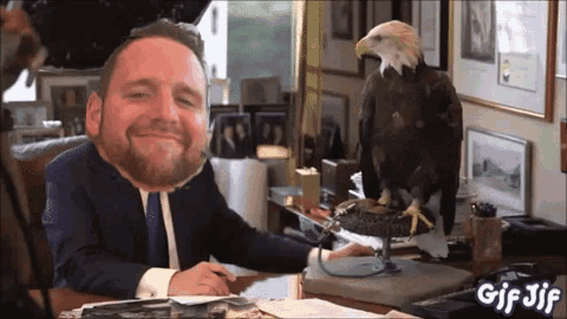 a man in a suit sits at a desk with a bald eagle sitting on top of it